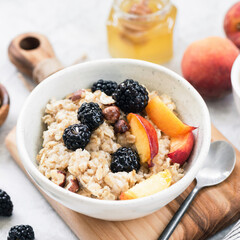 Oatmeal porridge bowl with hazelnuts, peach and blackberry served with cup of coffee. Healthy breakfast, healthy eating, dieting concept