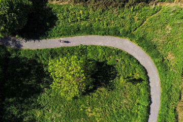 Aerial top down view on a footpath in a park with a man walking and casting strong shadow on the...