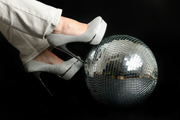 Women's foot in a formal shoe leaning against a disco ball on a black background