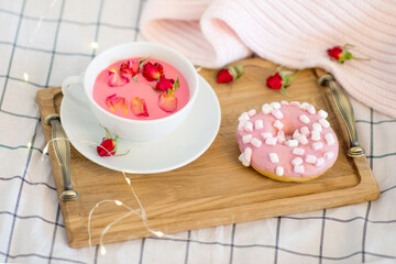 Fototapeta na wymiar pink breakfast in bed, donut and moonlit pink milk with pink flowers, wooden tray on a white bed, romantic breakfast