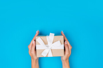 Top view of female hands holding a present box package in palms, on blue background