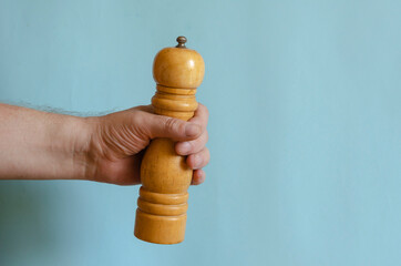 Adult man holds in his hand a wooden pepper mill.