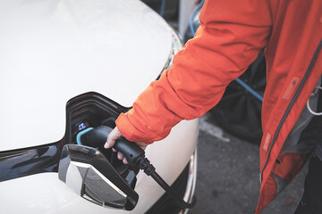 Human hand is holding Electric Car Charging connect to Electric car.