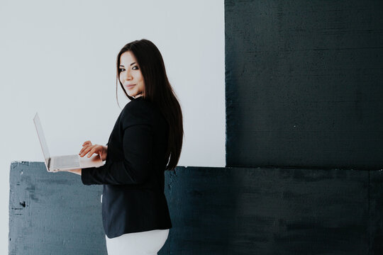 Beautiful brunette woman in white and black business business clothes in the office with a laptop
