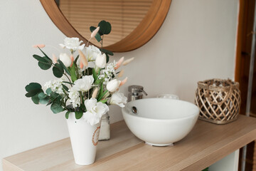 Artificial flowers in the bathroom interior. Decorative flowers in the bathroom. Artificial flowers in a vase. White bathroom interior. Decorative flowers. 