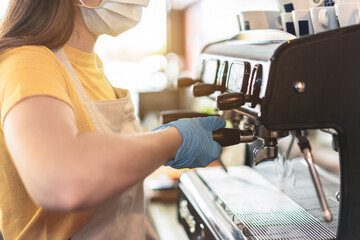Young female working inside breakfast bakery while making coffee wearing gloves and face mask for coronavirus spread prevention - Protective measures at work during Covid-19 outbreak - Focus on hand