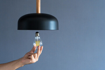 Close-up. A hand changes a light bulb in a stylish loft lamp. Spiral filament lamp. Modern interior...