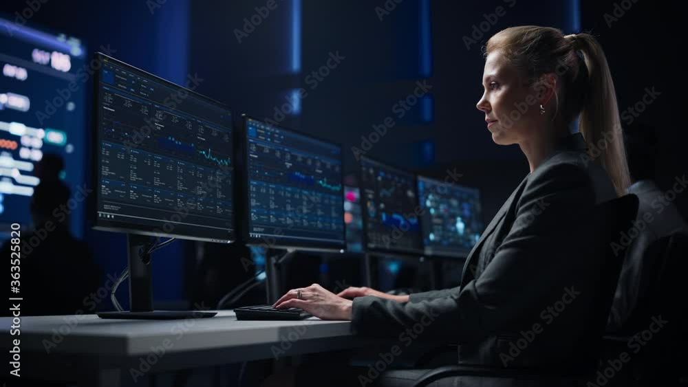 Poster confident female data scientist works on personal computer in big infrastructure control room. stock