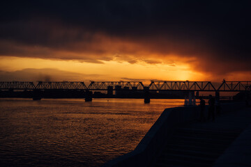 Fototapeta na wymiar Urban evening landscape. Railway bridge over the river at sunset. Fantastic clouds in the dark sky.