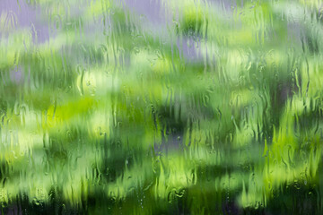 Water flowing on clear glass window with green background.