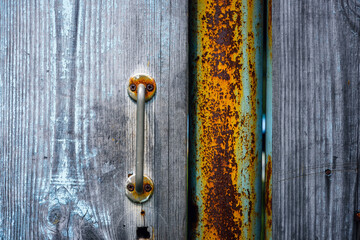 Fragment of an old wooden door with a rusty metal handle. Village gate, close-up.