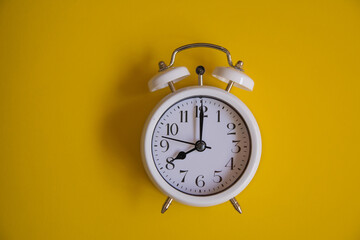 Vintage alarm clock with old white bells, with yellow background. Concept of a retro watch. Copy space