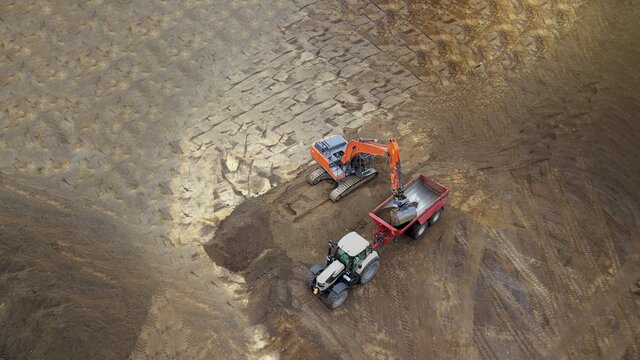 Baustelle: Tiefbau Erdbau Bauarbeiten: Bagger verlädt Erde, Sand auf einen Muldenkipper, Luftbild