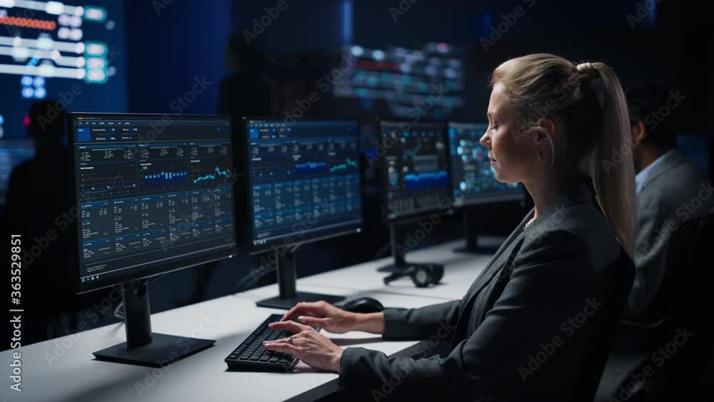 Poster confident female data scientist works on personal computer in big infrastructure control room. stock