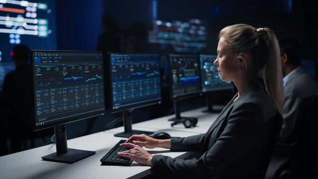 Confident Female Data Scientist Works on Personal Computer in Big Infrastructure Control Room. Stock Market Woman Specialist Uses Computer Showing Graphs, Charts, Information. Monitoring Room Team