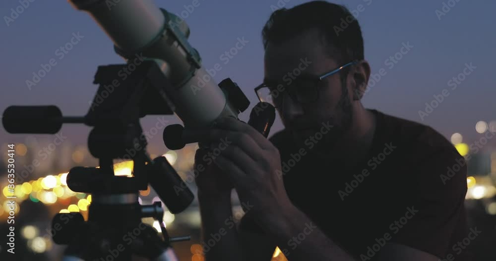 Wall mural astronomer with a telescope watching at the stars and moon with blurred city lights in the backgroun