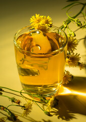 A glass of drink, teas, yellow daisies on a table