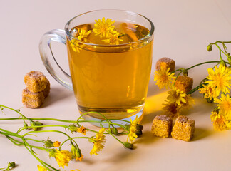 A glass of drink, teas, yellow daisies, sugar cubes on the table