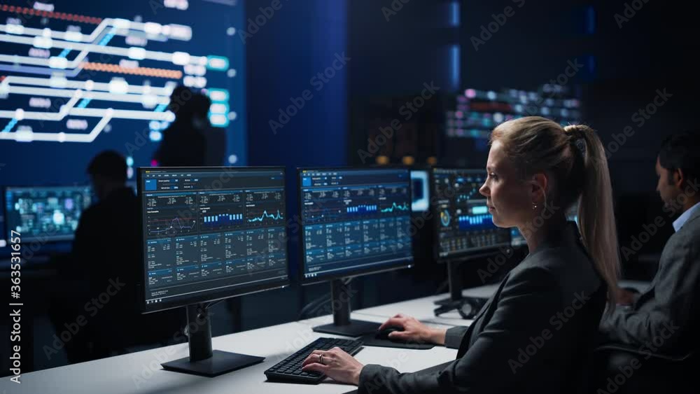 Poster confident female data scientist works on personal computer in big infrastructure control room. stock