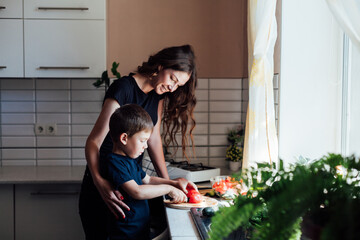 Little son helps mom cook vegetable salad cuts vegetables in kitchen