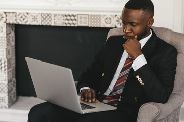  black businessman sitting in a chair in thought with a laptop in his hands