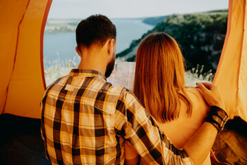 Couple of man and woman sitting in a tent, looking to a map, shot from the back.