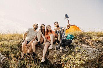 Group of friends filming a video blog, sitting on a cliff in mountains. Domestic travel concept.