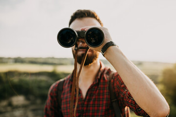 Young hipster man with binoculars standing in mountains, watching landscapes.