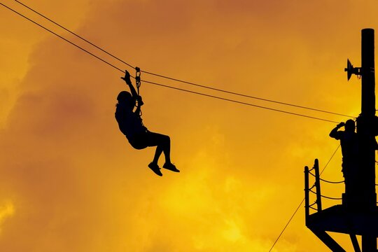 Low Angle View Of Silhouette Woman Ziplining Against Sky During Sunset