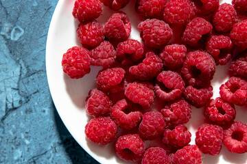 a lot of sweet fresh red raspberries on a plate from the market or garden