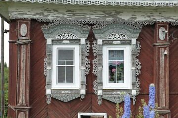 Richly decorated ornamental carved windows and frames on vintage wooden rural house in village in Ivanovo region, Russia. Russian traditional national folk style in wooden architecture. Countryside