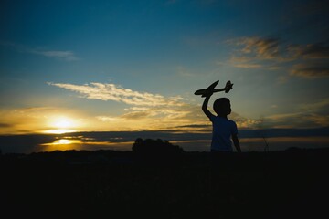 Kid boy playing with toy plane during sunset time. Childhood memories - beautiful sky over meadow. Childhood dream imagination concept