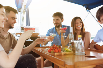 Group of happy friends drinking vodka cocktails at boat party outdoor, cheerful and happy. Young people having fun in sea tour, youth and summer vacation concept. Alcohol, vacation, resting.