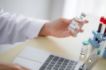 Asian female doctor holding bottle of exam vaccine in hospital. Medical treatment data collection.