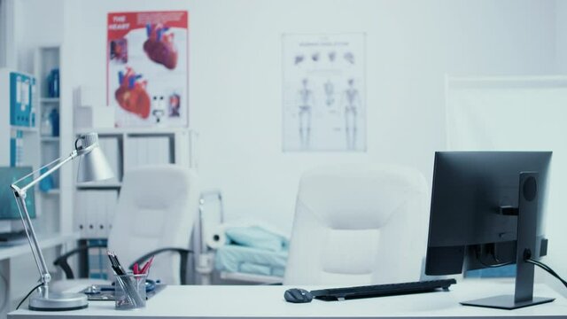 Modern medical consultation office with nobody in it. Hospital private clinic room with glass walls, computers on front desk healthcare system clean medicine cabinet. Treatment equipment and