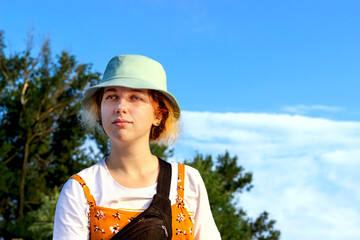 Close-up of a cute hipster girl looking thoughtfully dreamily towards nature, Park, forest, against the blue sky. She's wearing a white t-shirt and a blue Panama hat. Summer outdoor recreation