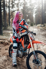 Fototapeta na wymiar Beautiful racer girl with pink hair in motocross kit sitting on her motorcycle in off road adventure