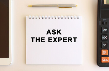Notepad with text ASK THE EXPERT on a white background, near calculator, tablet and pen. Business concept.