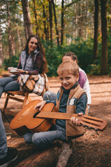 Happy family on a camping trip relaxing in the autumn forest. A boy holds a guitar in his hands