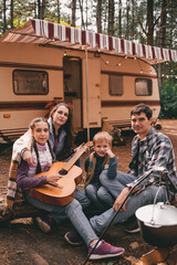 Happy family on a camping trip relaxing in the autumn forest. Camper trailer. Fall season outdoors trip