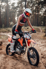Modern young female motocross racer with pink hair in safety helmet riding on her motorcycle in off...
