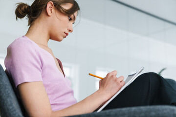 Photo of serious woman making sketch or notes while sitting on armchair