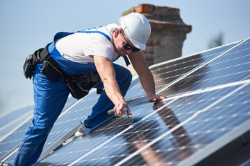 Male workers installing stand-alone solar photovoltaic panel system. Electricians mounting blue solar module on roof of modern house. Alternative energy ecological concept.