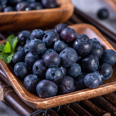 Pile of blueberry fruit in a bowl plate on a tray over gray cement concrete background, close up, healthy eating design concept.