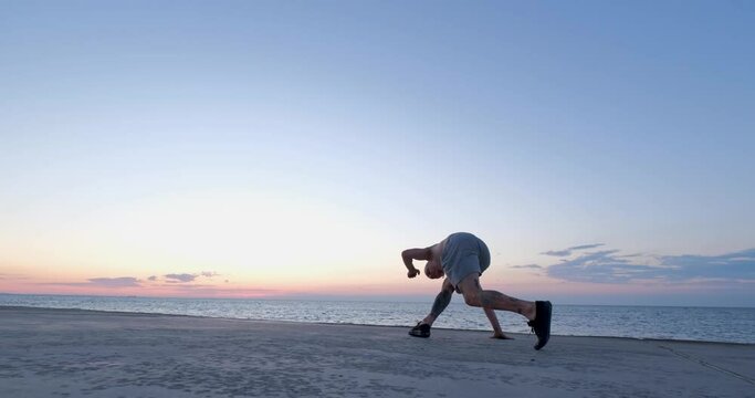 Male training capoeira acrobatick tricks on the beach during sunset, dancer near the sea 