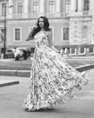 Outdoor fashion female portrait. Elegant woman in long ball gown dress. Caucaisan brunette woman with wavy hair. Girl walking city street