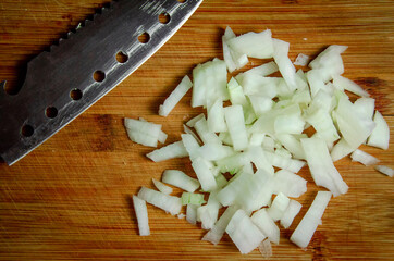 white fresh raw onions chopped finely with a large knife on a wooden plate close-up top view