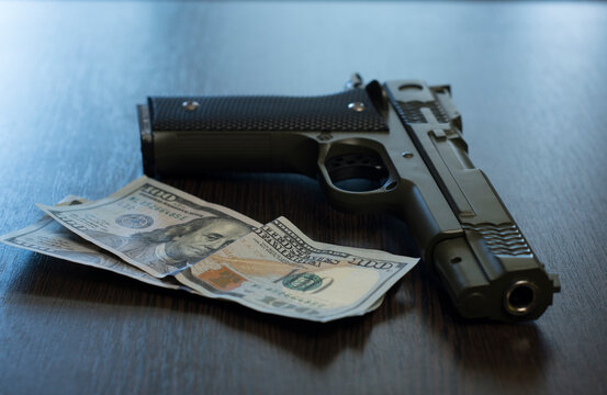 Khaki pistol and two hundred dollar bills lie on a wooden table. Close-up