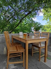 Outdoor terrace of restaurant and green trees background. Empty street patio restaurant, wooden table and chairs without people. Glass of beer on the table. Cafe of the old Soviet style, Moscow, VDNH.