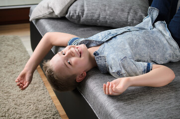 Cute funny boy lying upside down on sofa looking at camera, smiling playful child boy having fun at...